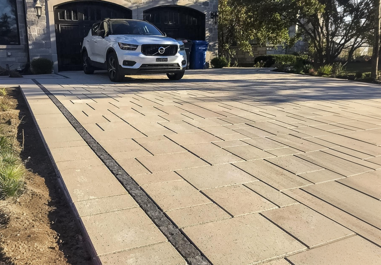 Residential driveway with beige interlocking pavers, linear accent design, and premium finish