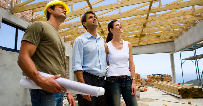 Contractor and homeowners observing the wood framing of a house under construction on a residential worksite.