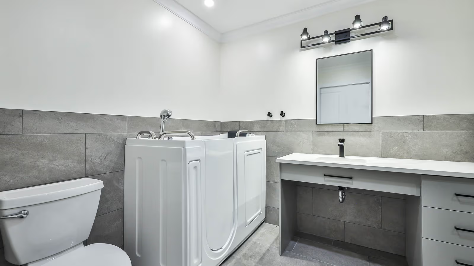 Accessible bathroom with walk-in bathtub, gray tile, white vanity and black fixtures