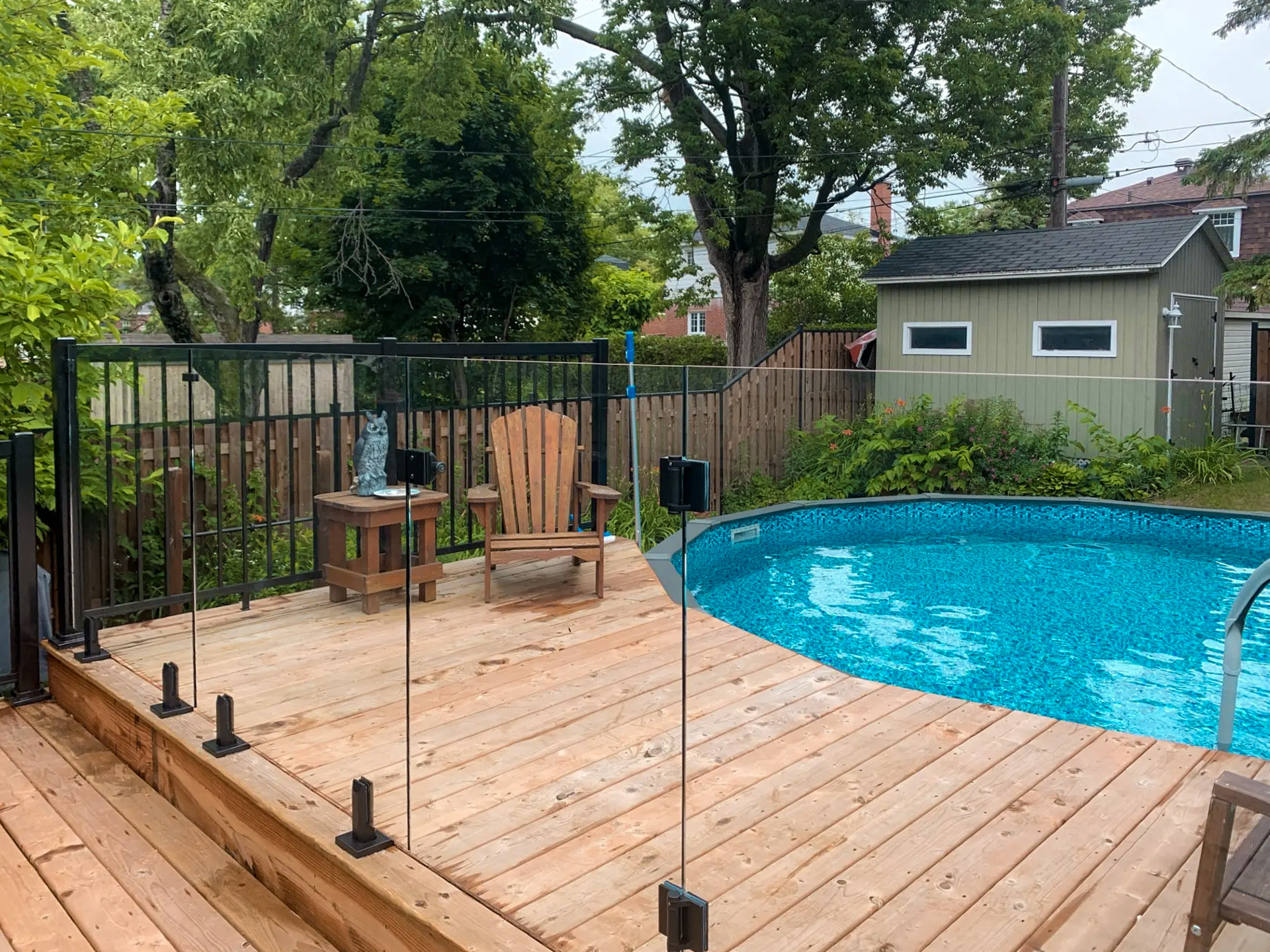 Wooden deck with glass fence and above ground pool in a residential yard