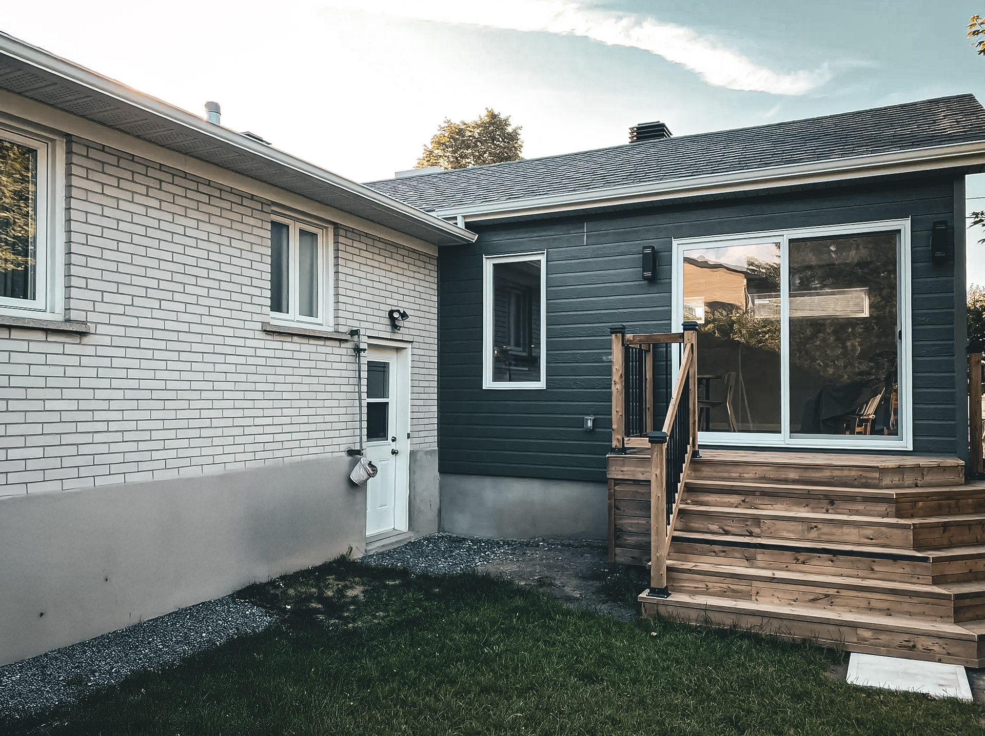 Exterior renovation with modern facade cladding, wooden patio and contemporary windows, offering a warm and functional exterior design.