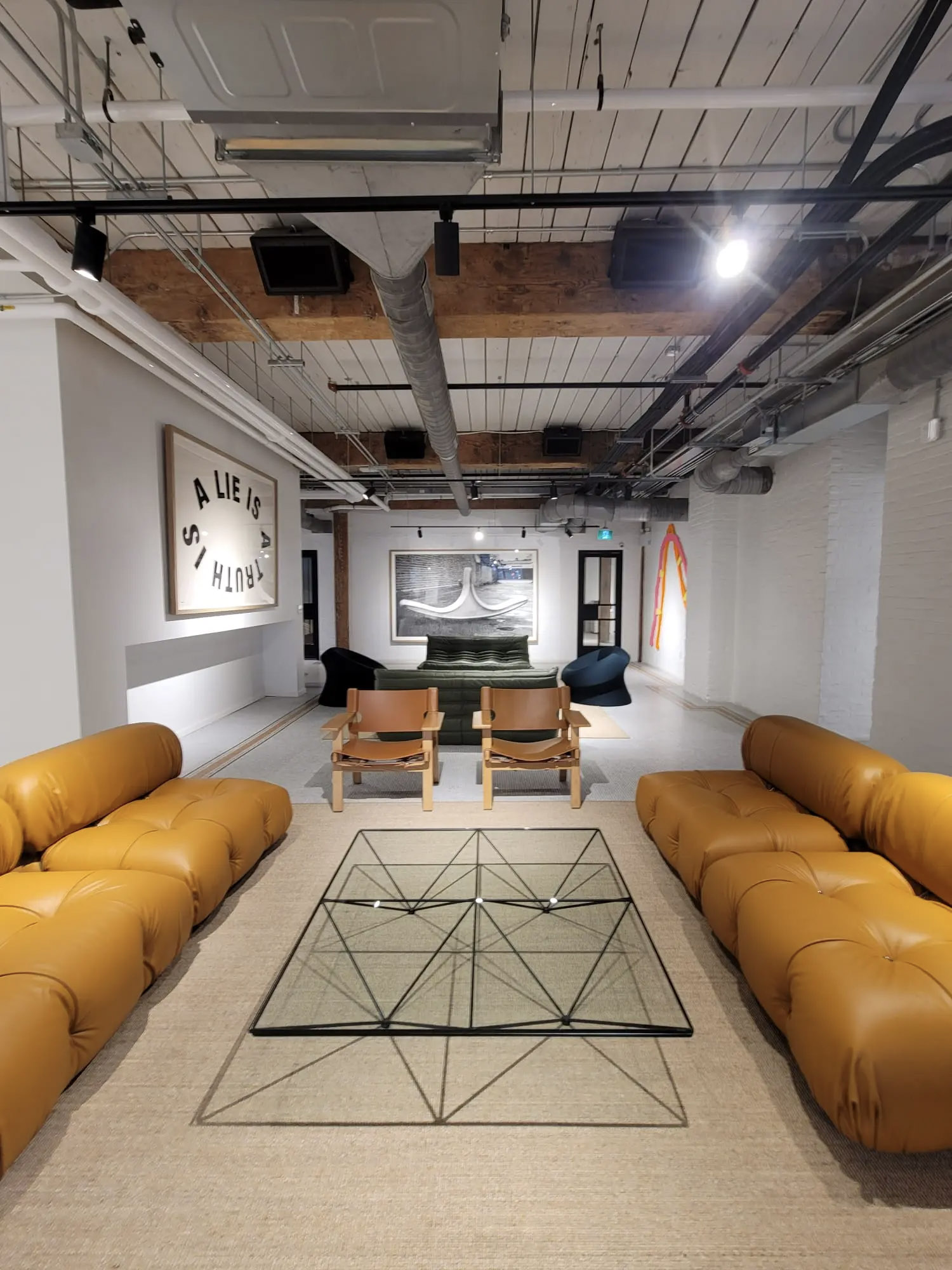 Stylish industrial-design living room with exposed beam ceiling, contemporary camel leather furniture, geometric glass coffee table, and modern wall art.