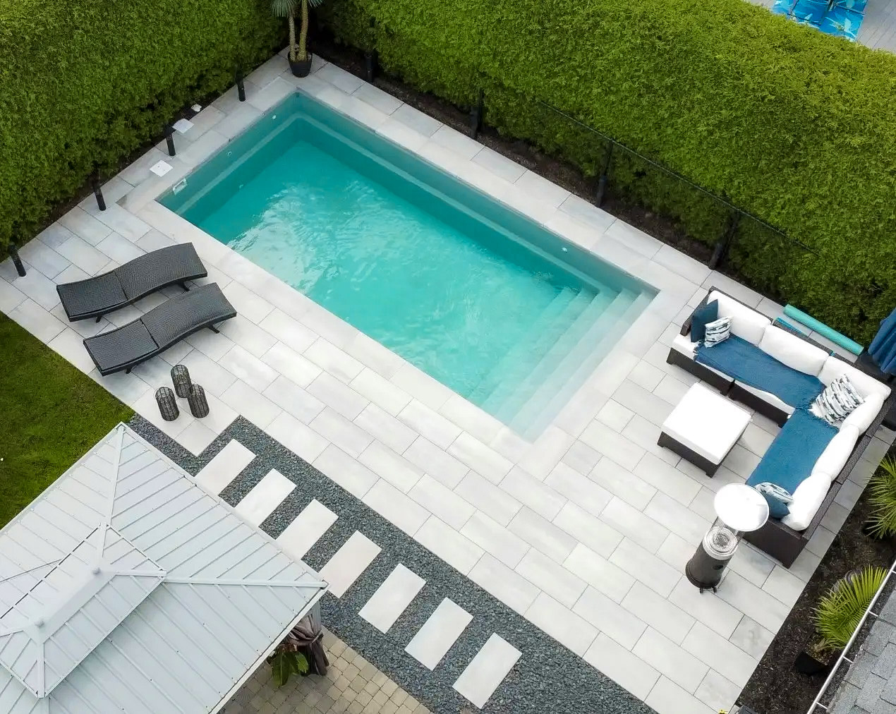 Vue aérienne d'une cour arrière aménagée avec piscine creusée, pavés modernes, mobilier de jardin et haies de cèdres