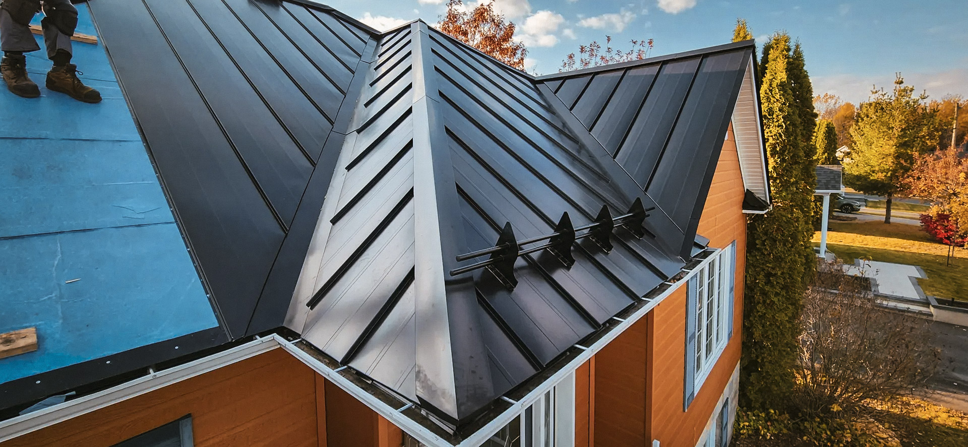 Installation of a black standing-seam metal roof with valleys, ridges, and snow guards on a residential house.