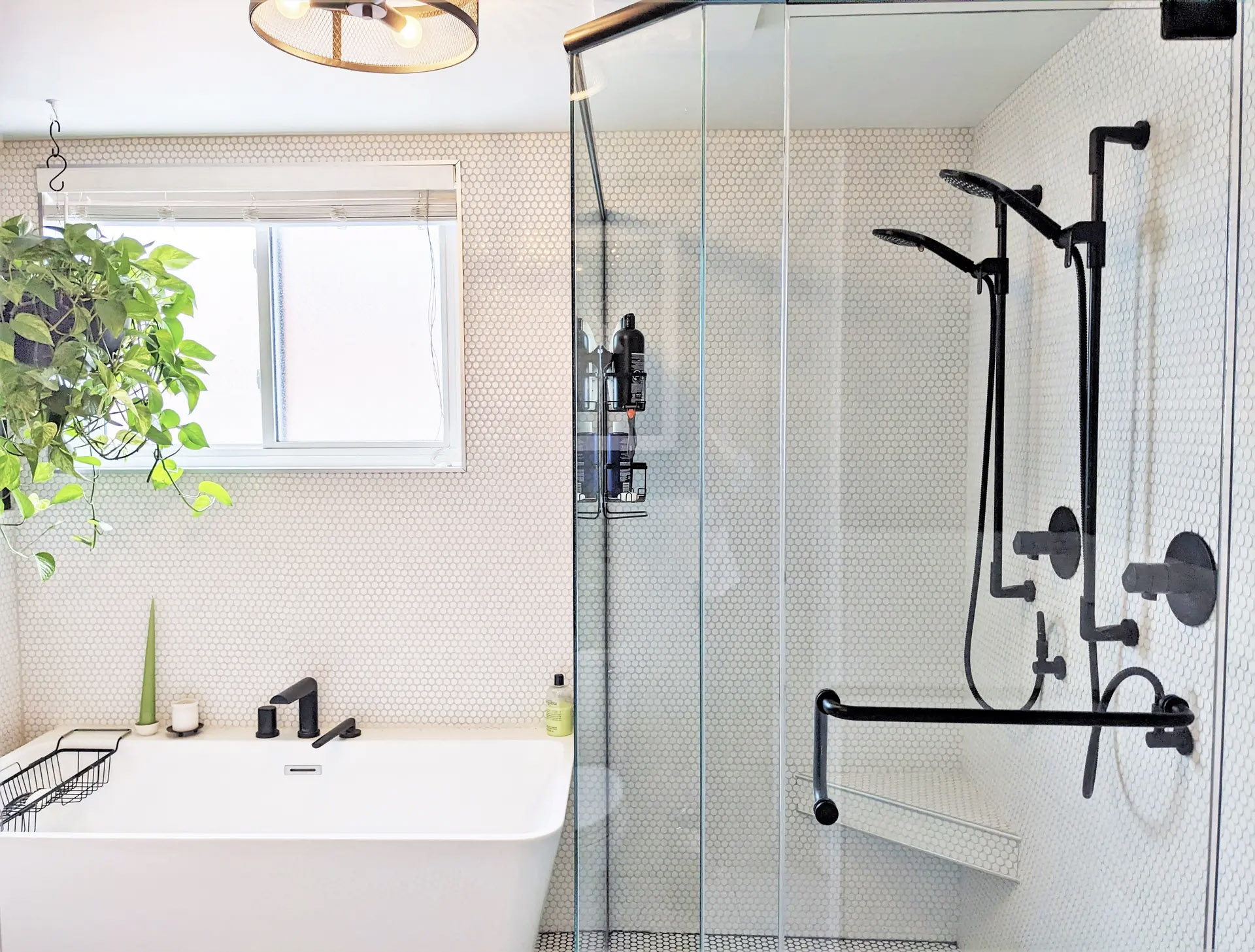 Bright and modern bathroom with white bathtub, glass shower, round mosaic tiles, black faucets, window, hanging plant and decorative lighting for a fresh and refined atmosphere