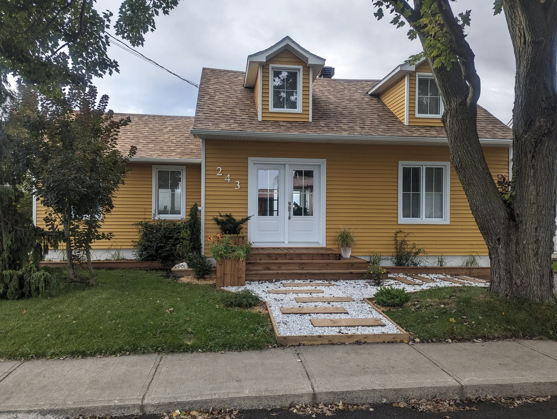 Yellow house with white doors, shingle roof, landscaping and decorative stone walkway.