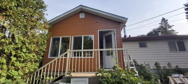 House facade with brown siding, white balcony, exterior staircase and large glass door.