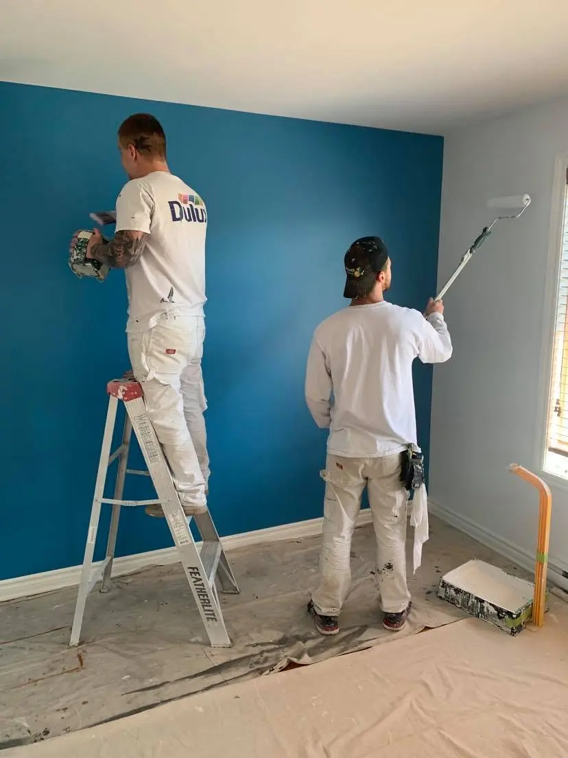 Interior painting work by professional painters applying blue paint on a wall for a modern renovation.