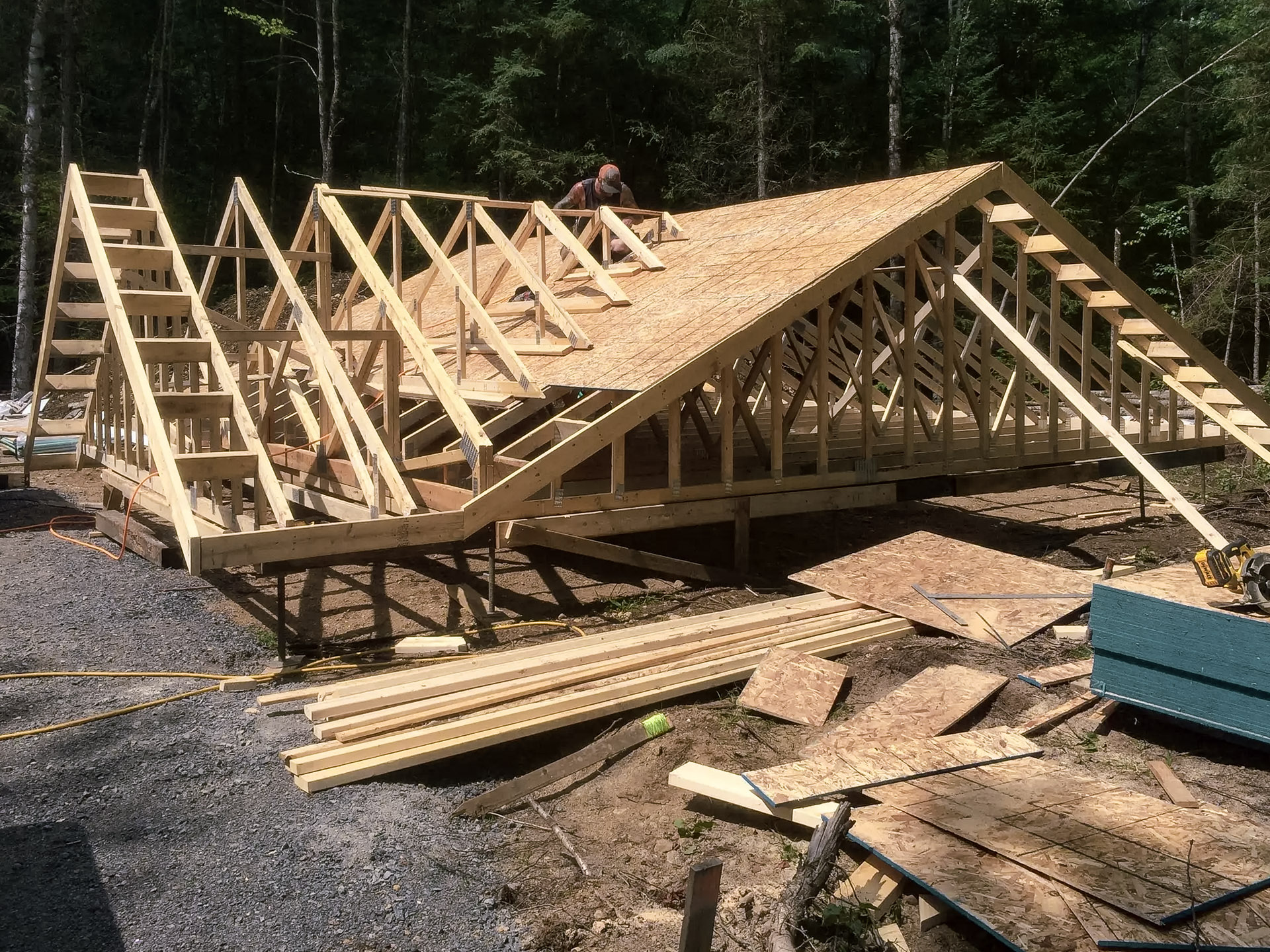 Wooden house frame construction with roof sheathing installation in a forested area