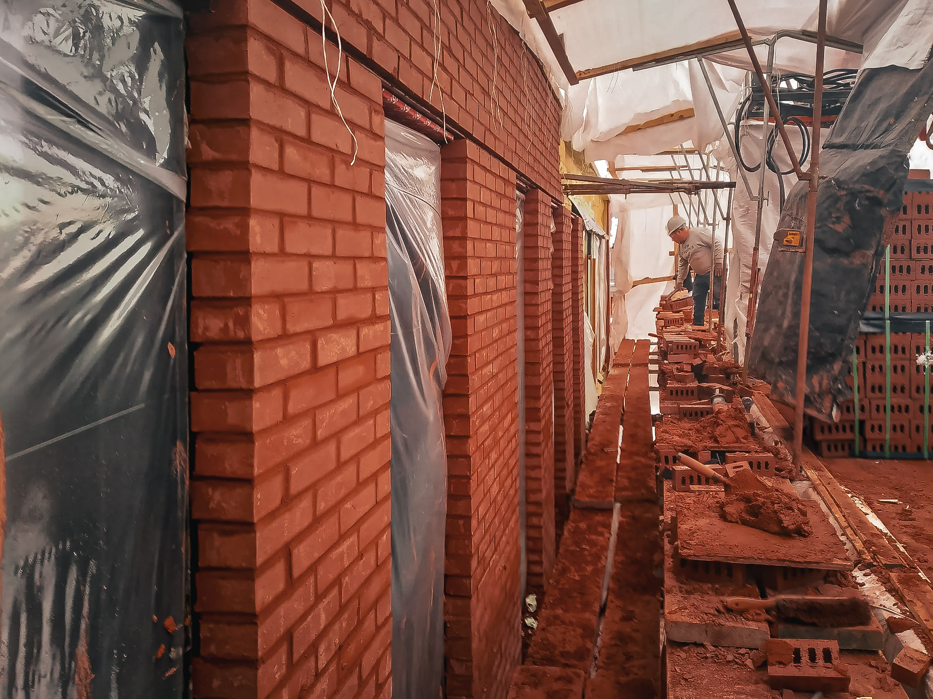 Exterior masonry work with red brick installation on a building façade, scaffolding, protected openings, and mortar joint finishing.