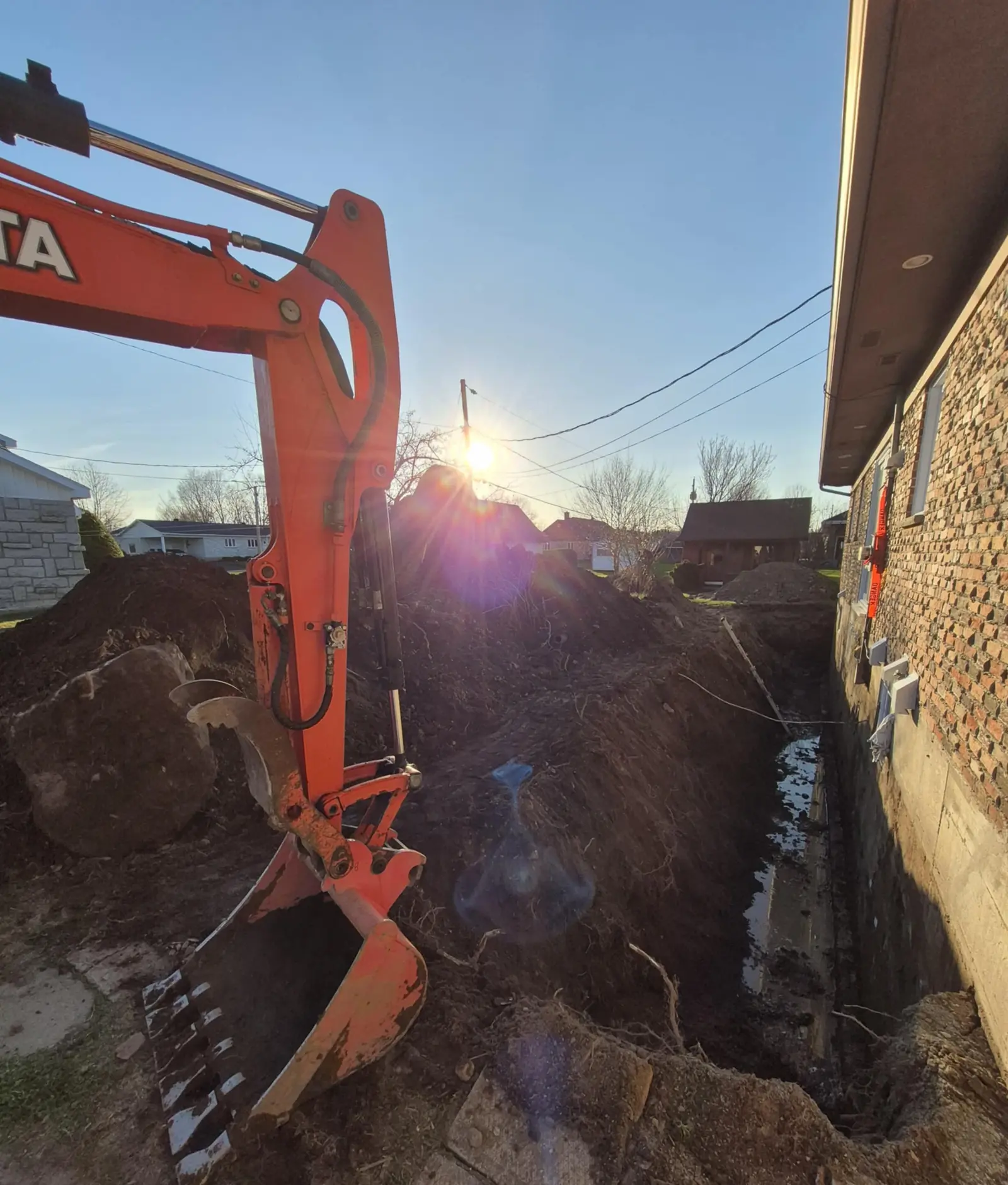 Excavator digging a trench along a house foundation for drainage or repair