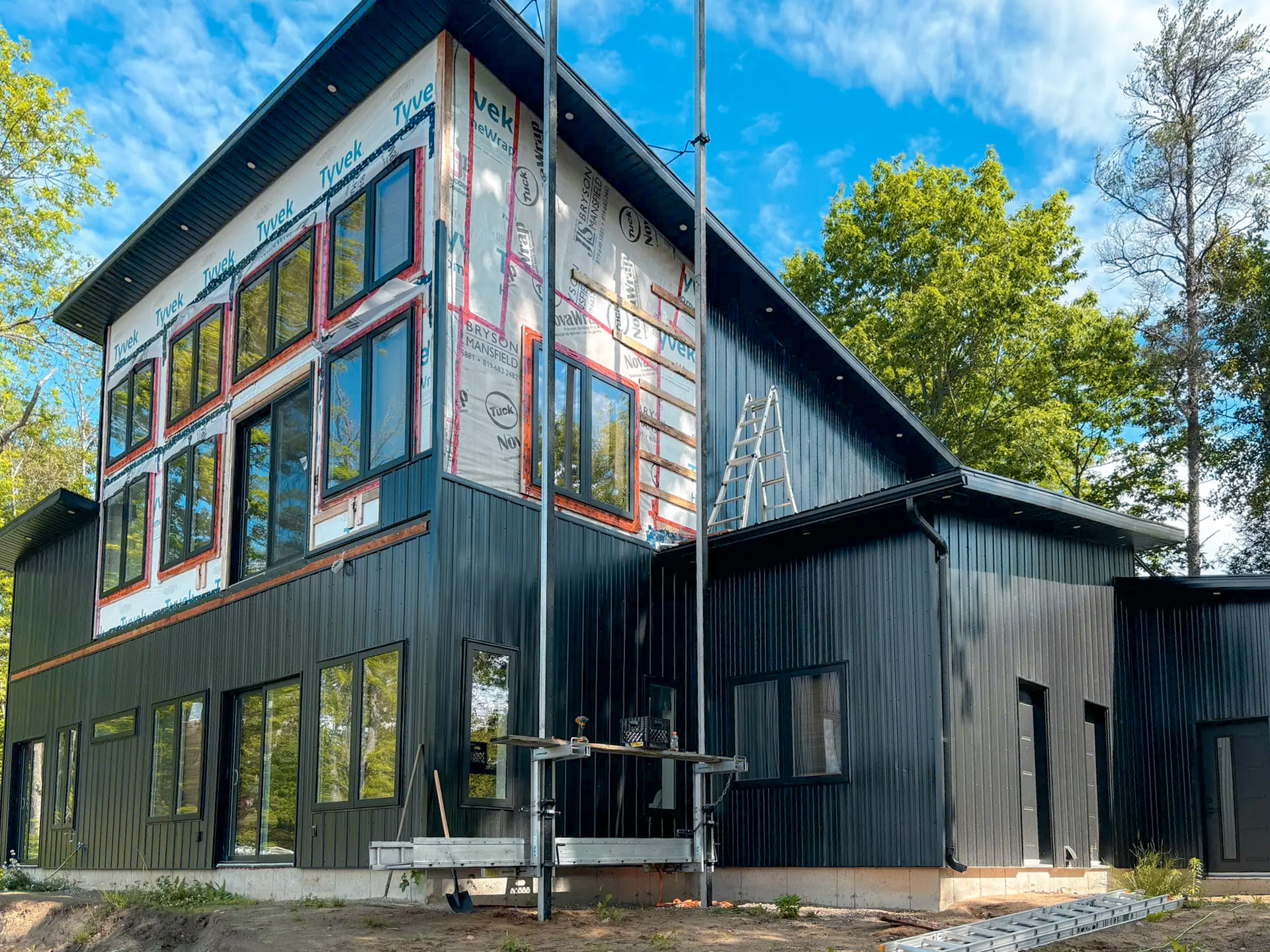 Maison contemporaine en construction avec revêtement métallique noir et isolation Tyvek partiellement exposée