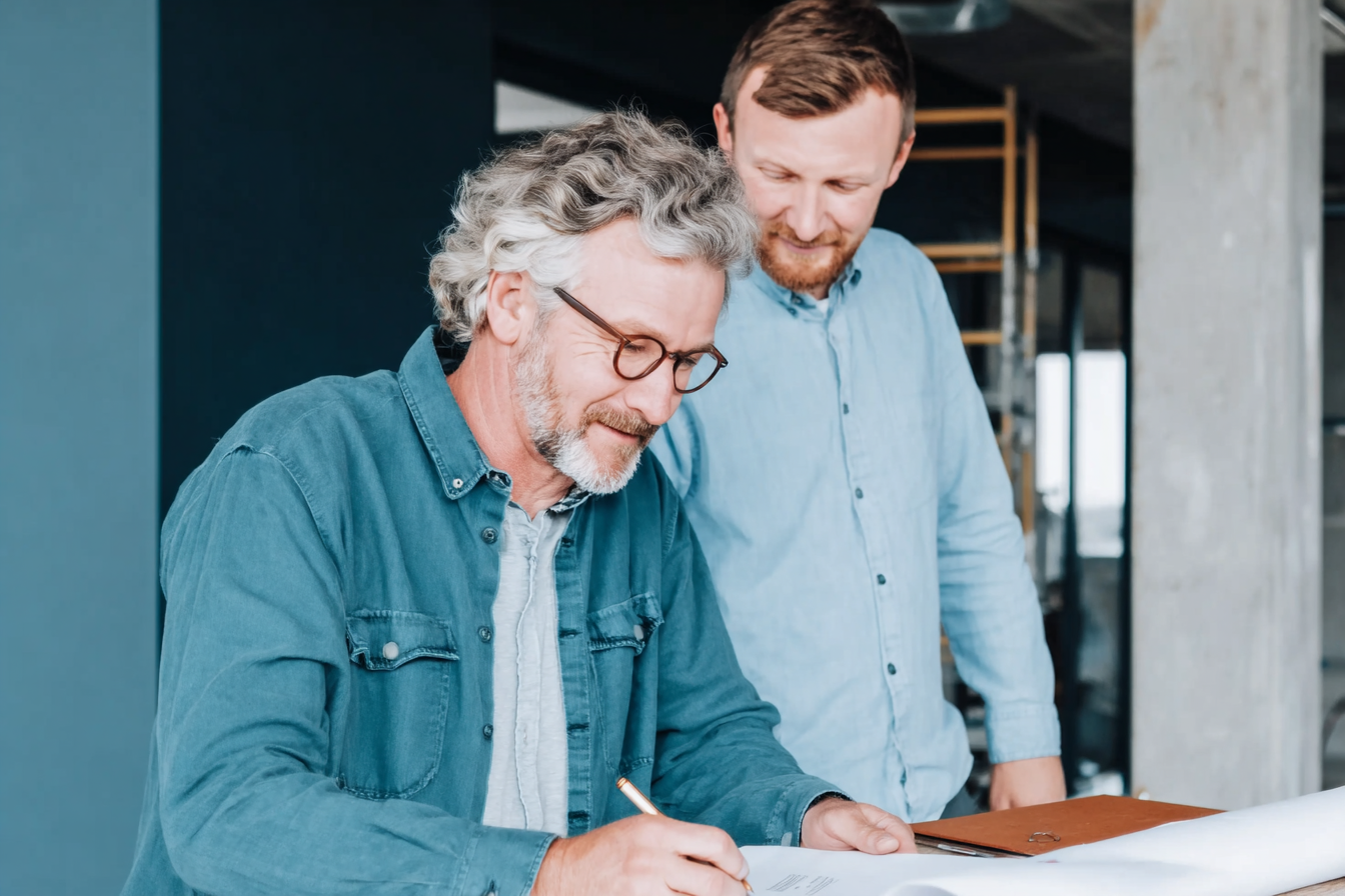 Two men in shirts discussing construction plans inside a building under construction