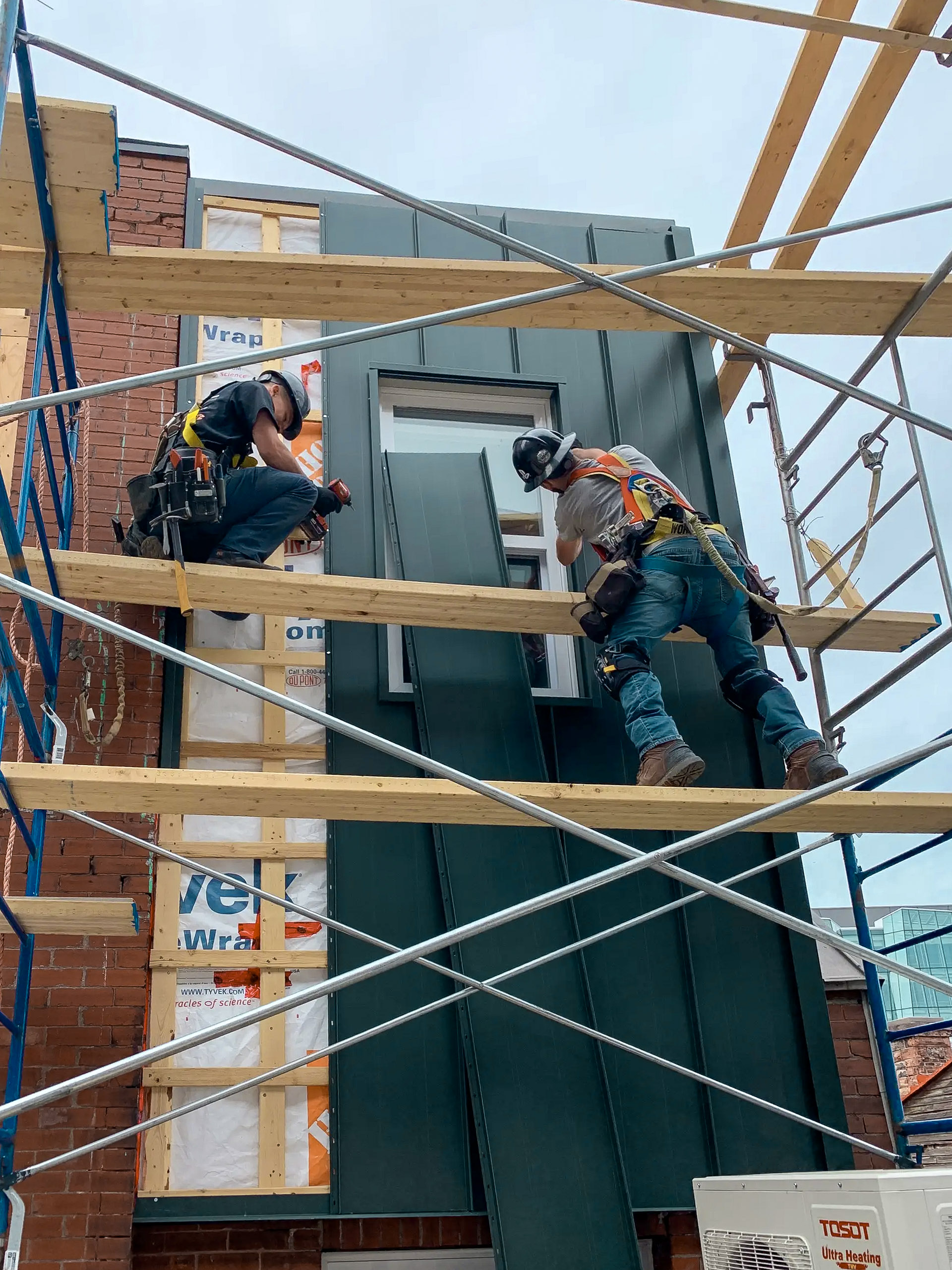 Travailleurs de la construction installant un revêtement métallique vertical sur la façade d’un bâtiment à l’aide d’un échafaudage