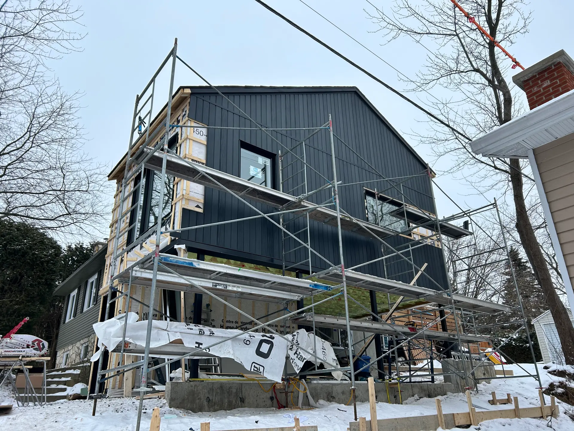 Maison en construction avec échafaudages et installation de revêtement extérieur vertical noir en hiver