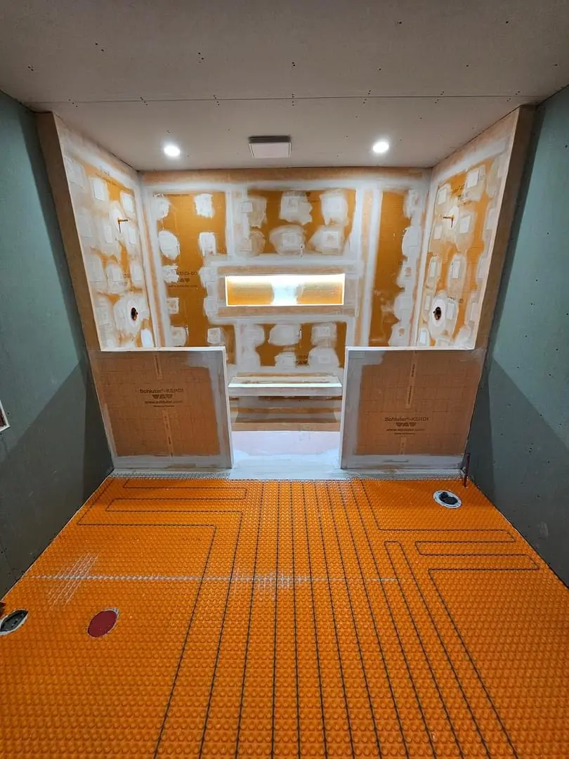 Salle de bain en préparation avec membrane d’étanchéité orange, panneaux muraux, joints tirés et plancher chauffant
