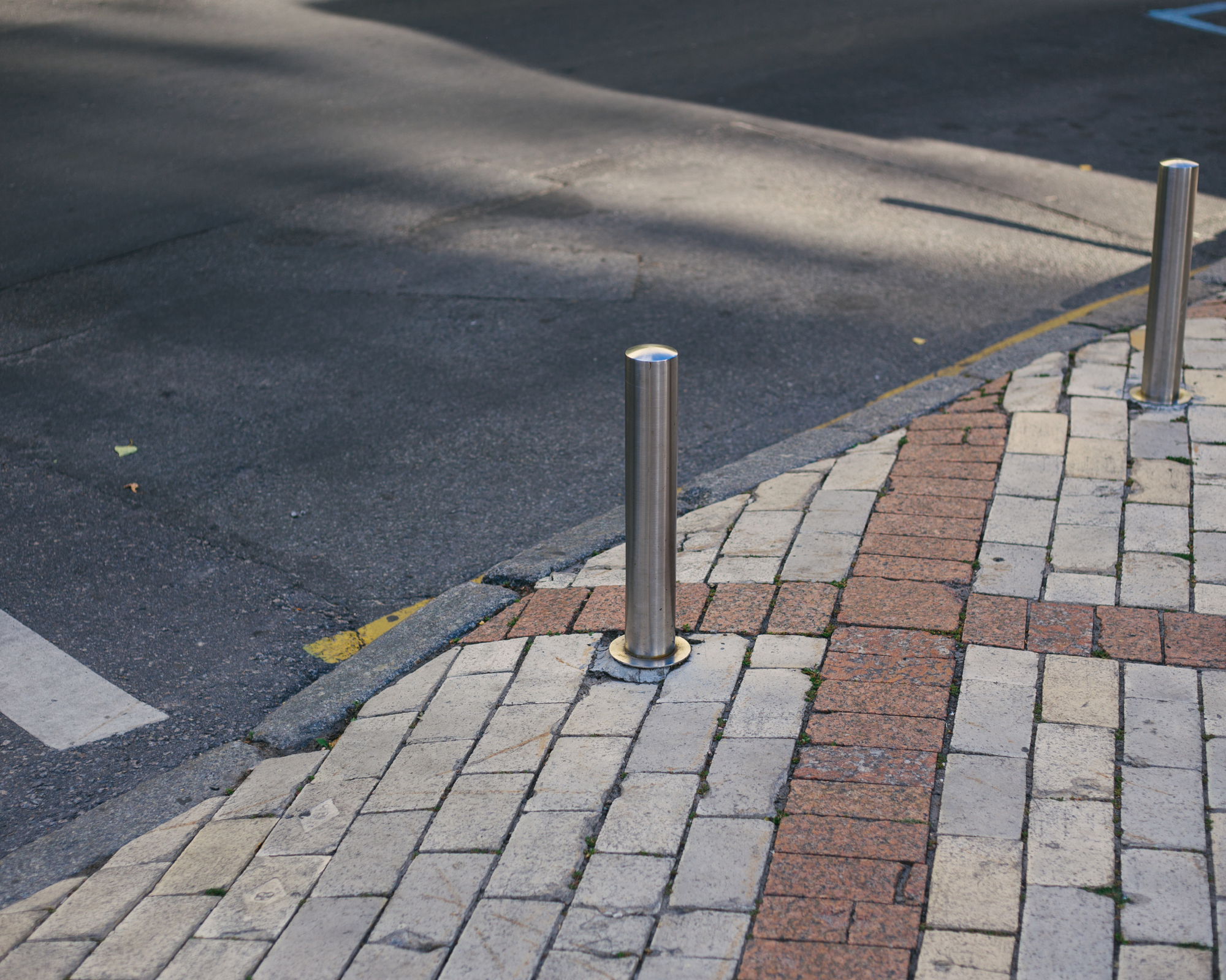 Stainless steel bollard installed at the edge of a paved sidewalk.