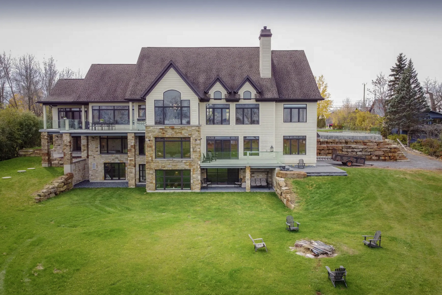 Rear view of a prestigious house on a sloping plot, with stone cladding, large panoramic windows and a spacious lawned garden<br>