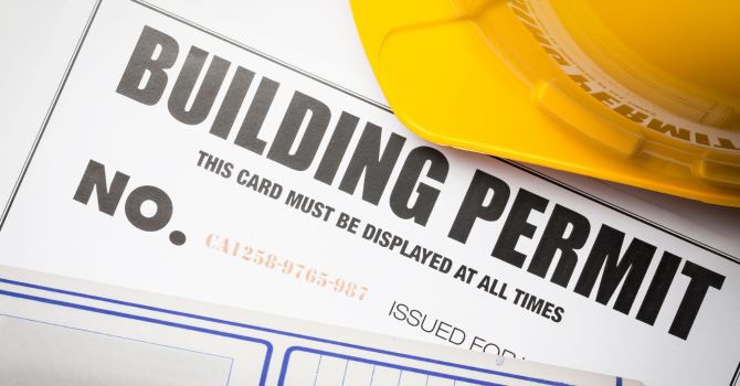 Official building permit with a yellow safety hard hat, representing construction permit requirements, regulatory compliance, and building project approval.