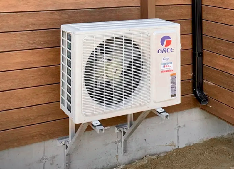 Unité extérieure de thermopompe Gree installée sur un mur en bois à l'aide d'un support métallique, avec un système de tuyauterie discret, illustrant une solution moderne et efficace pour le chauffage et la climatisation dans un cadre résidentiel.