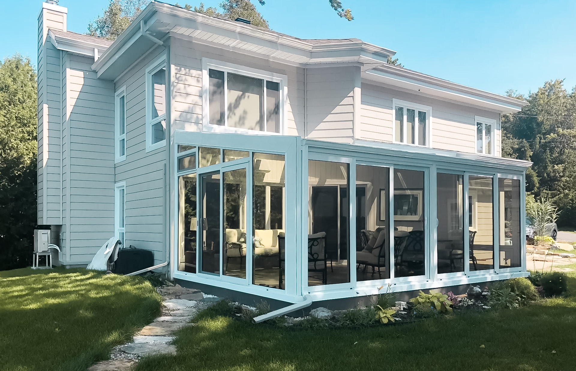 Modern house with a large glass-enclosed veranda, surrounded by greenery and carefully landscaped grounds.