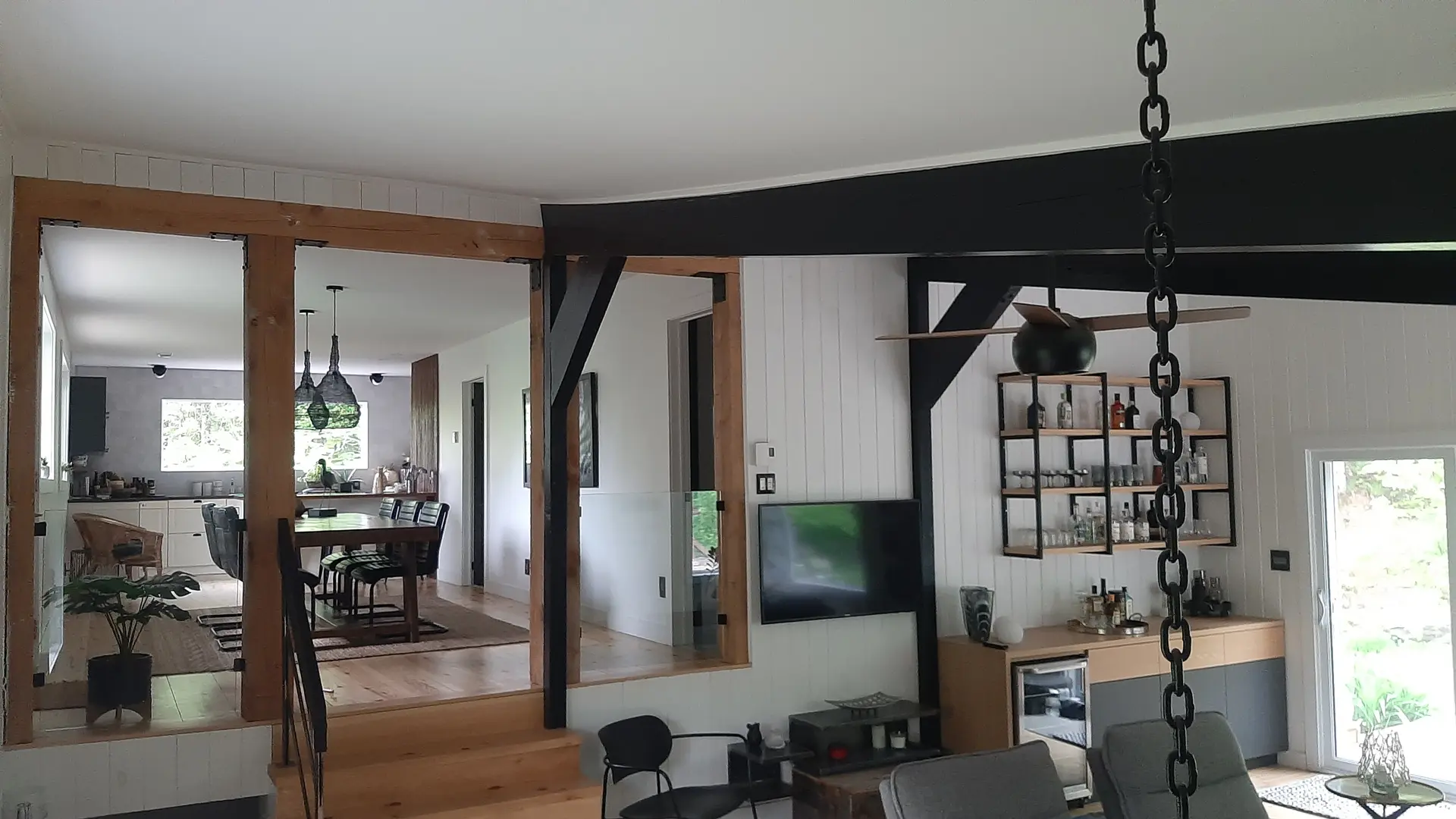 Renovated open-concept interior with black steel beam, wood posts, glass railing and built-in bar area