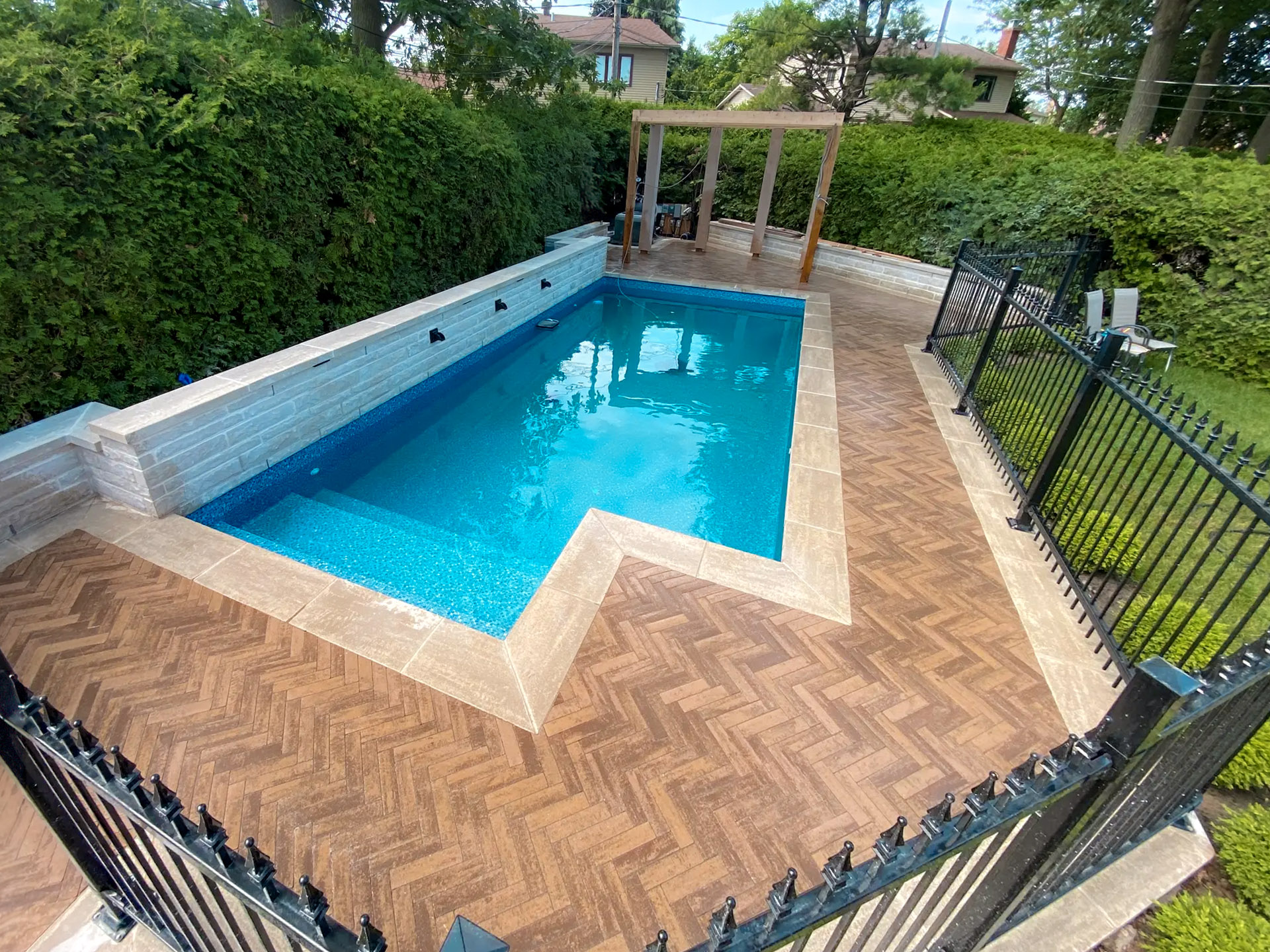 Inground pool with wood-effect ceramic deck and ornamental iron fence in a residential courtyard