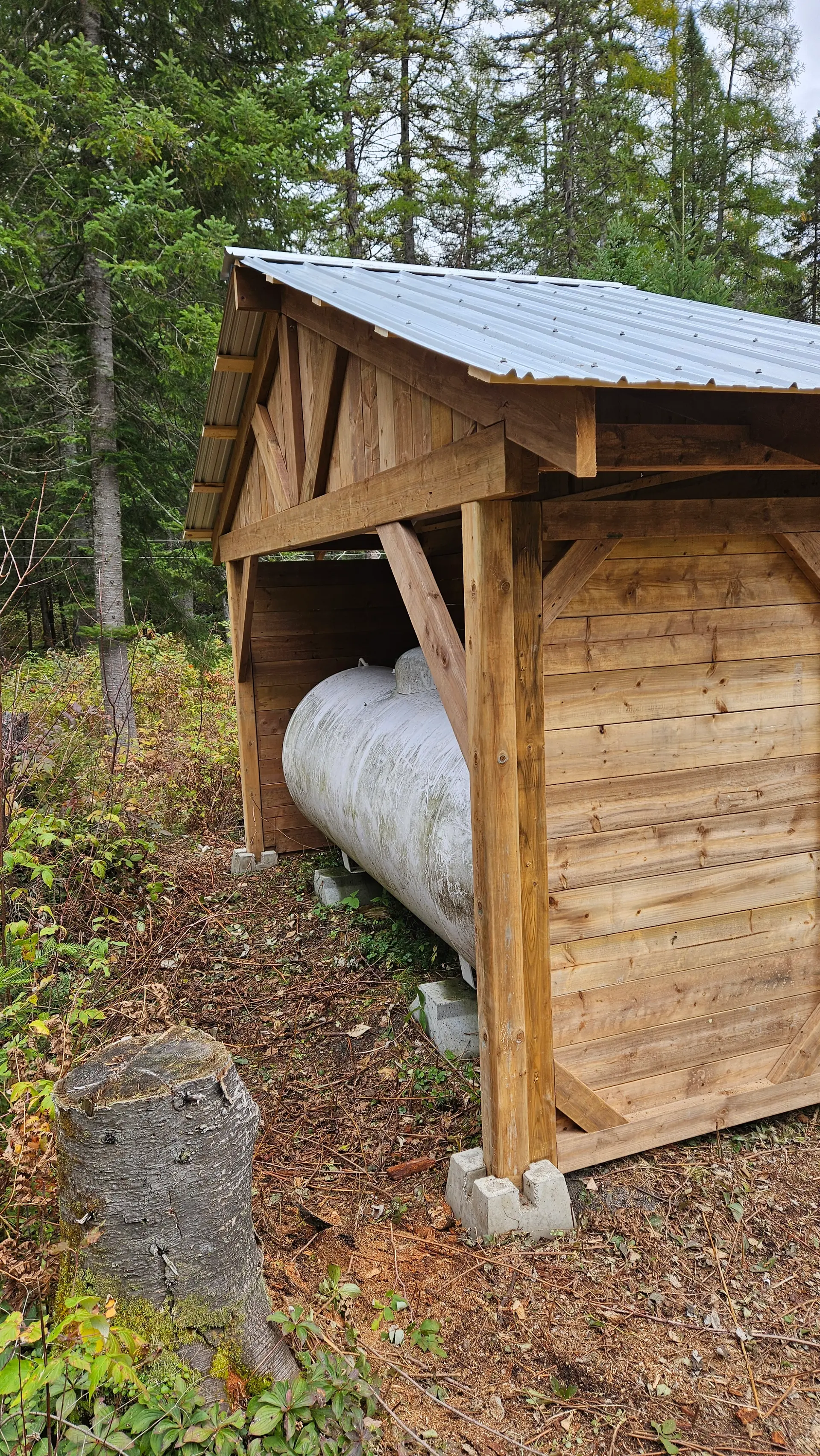 Wooden shelter with metal roof protecting an outdoor tank in a forest setting