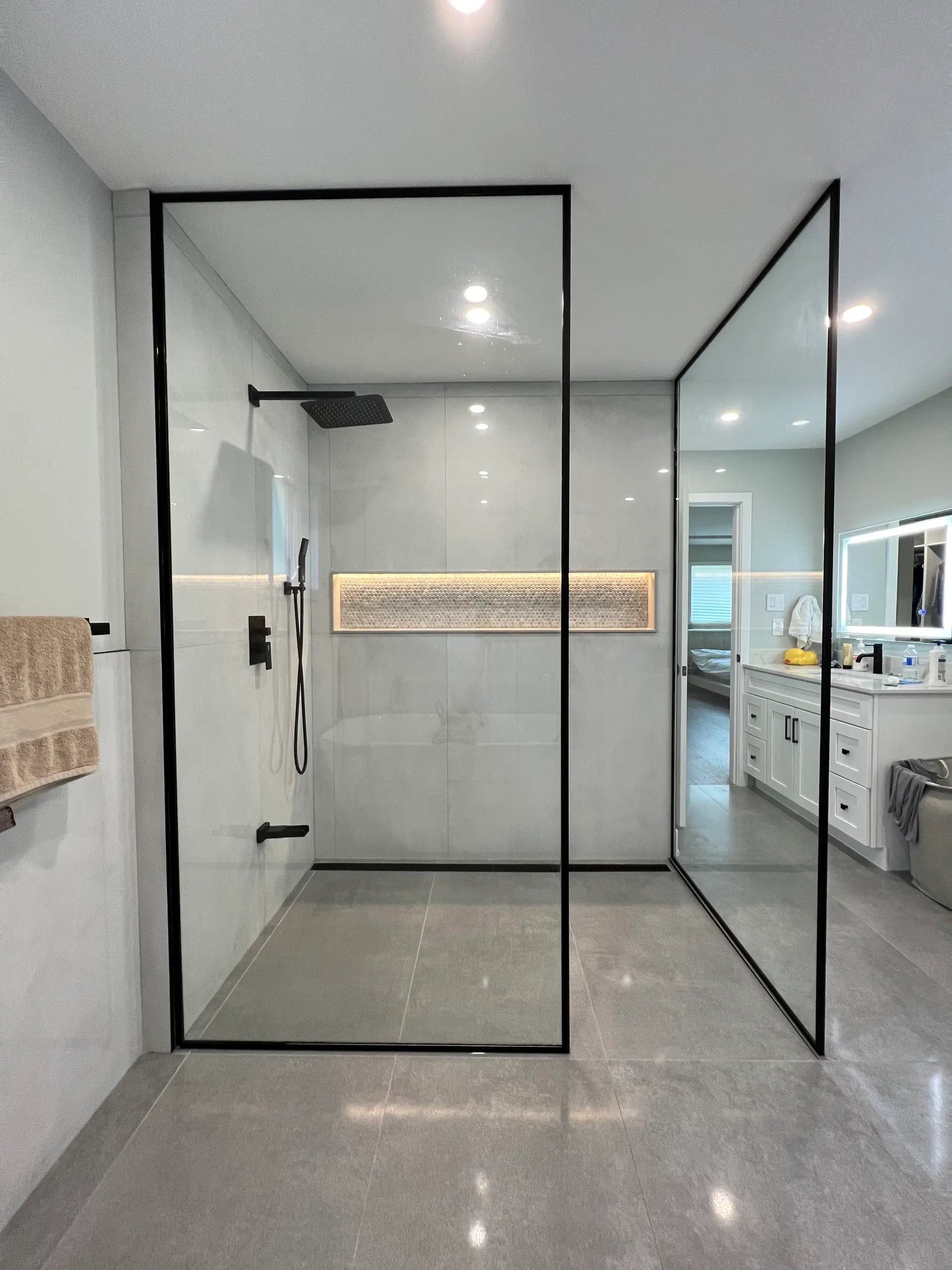 Modern walk-in shower with black-framed glass panels, large grey tiles, black fixtures, and an illuminated wall niche.