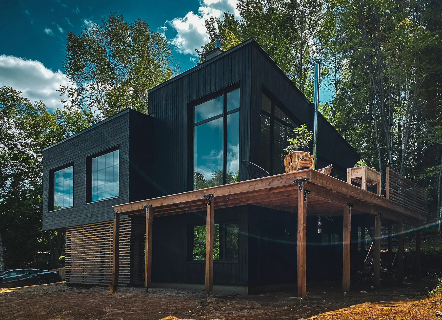 Modern black house with large windows and elevated wooden deck, surrounded by forest
