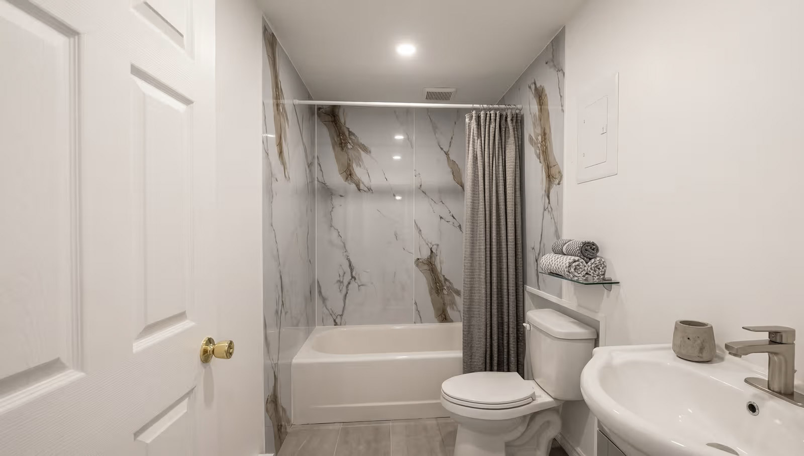 Salle de bain avec bain-douche et revêtement mural effet marbre avec rideau et vanité blanche
