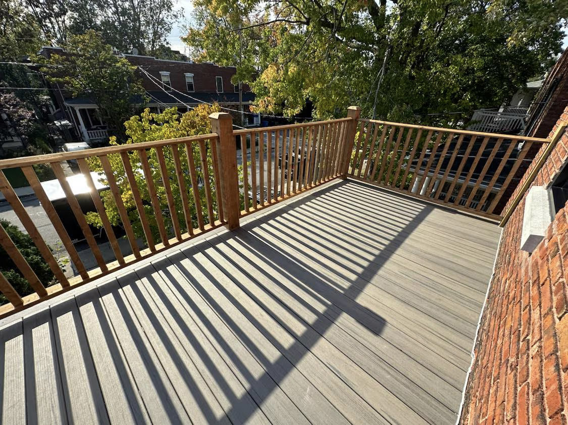 Grande terrasse extérieure avec plancher composite gris, garde-corps en bois et vue sur un quartier résidentiel arboré.