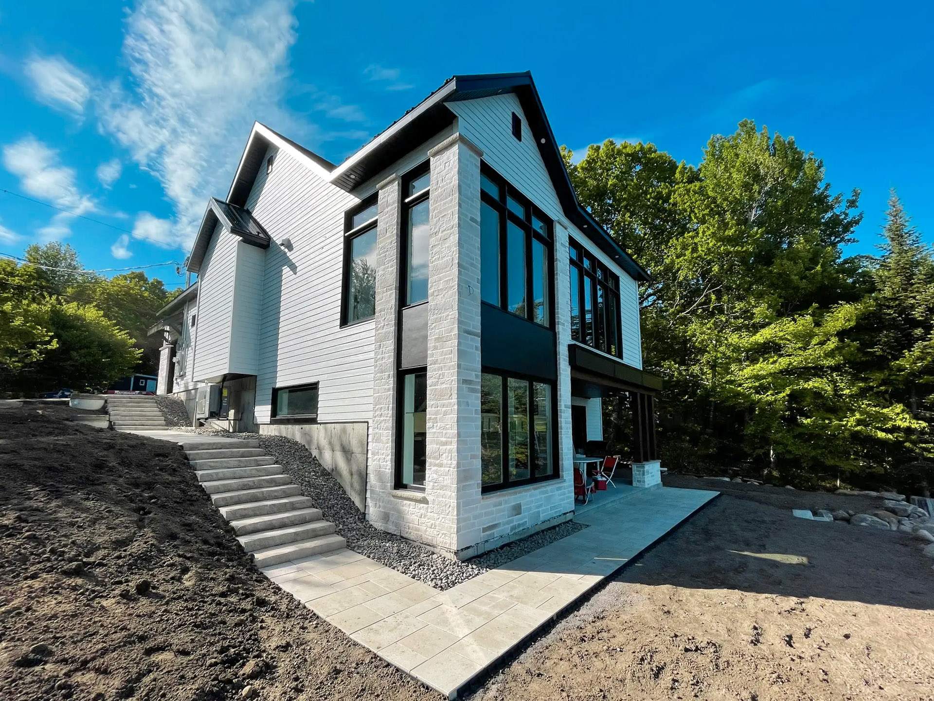 Contemporary house on the edge of a forest with a pale brick facade, large black windows and a staircase on a sloping plot