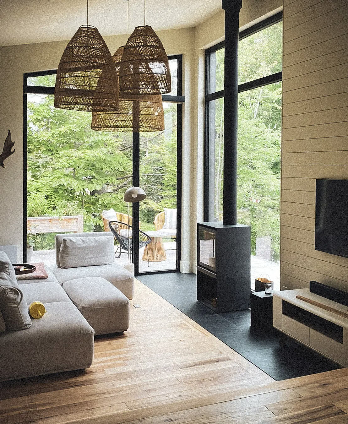 &nbsp;Salon moderne avec grandes fenêtres, poêle à bois, luminaires en rotin et mobilier contemporain en tissu