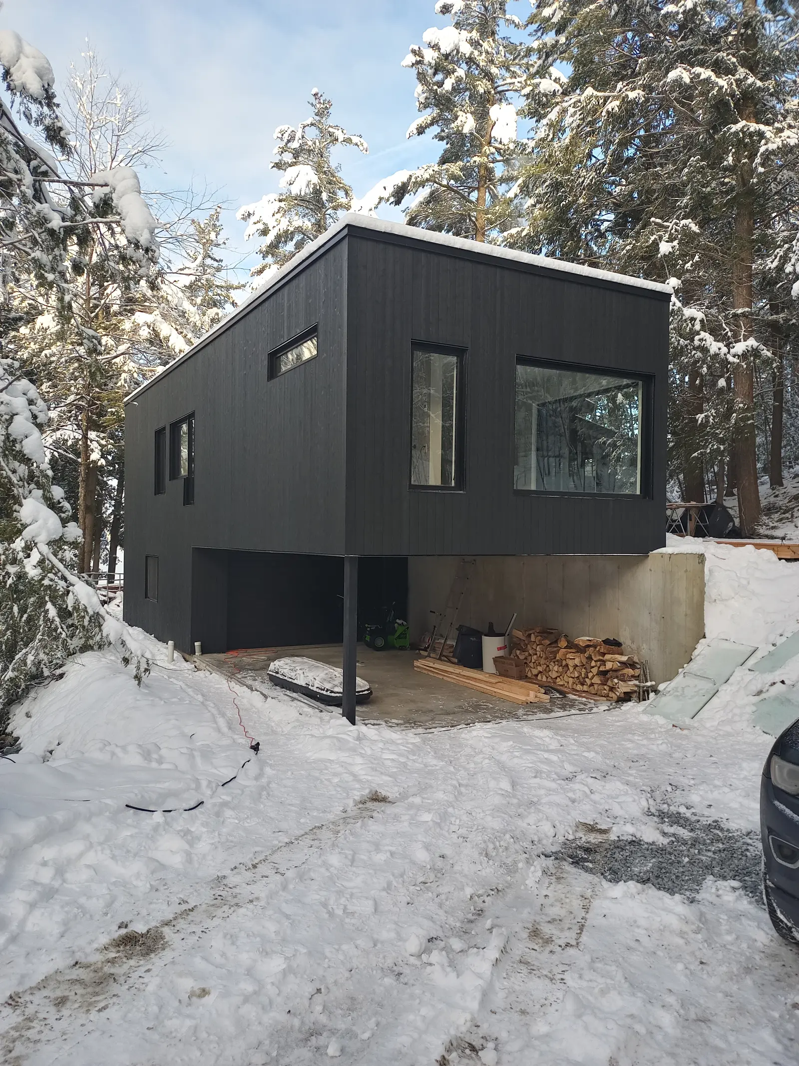 Modern black wood house on stilts with open basement, located in snowy forest