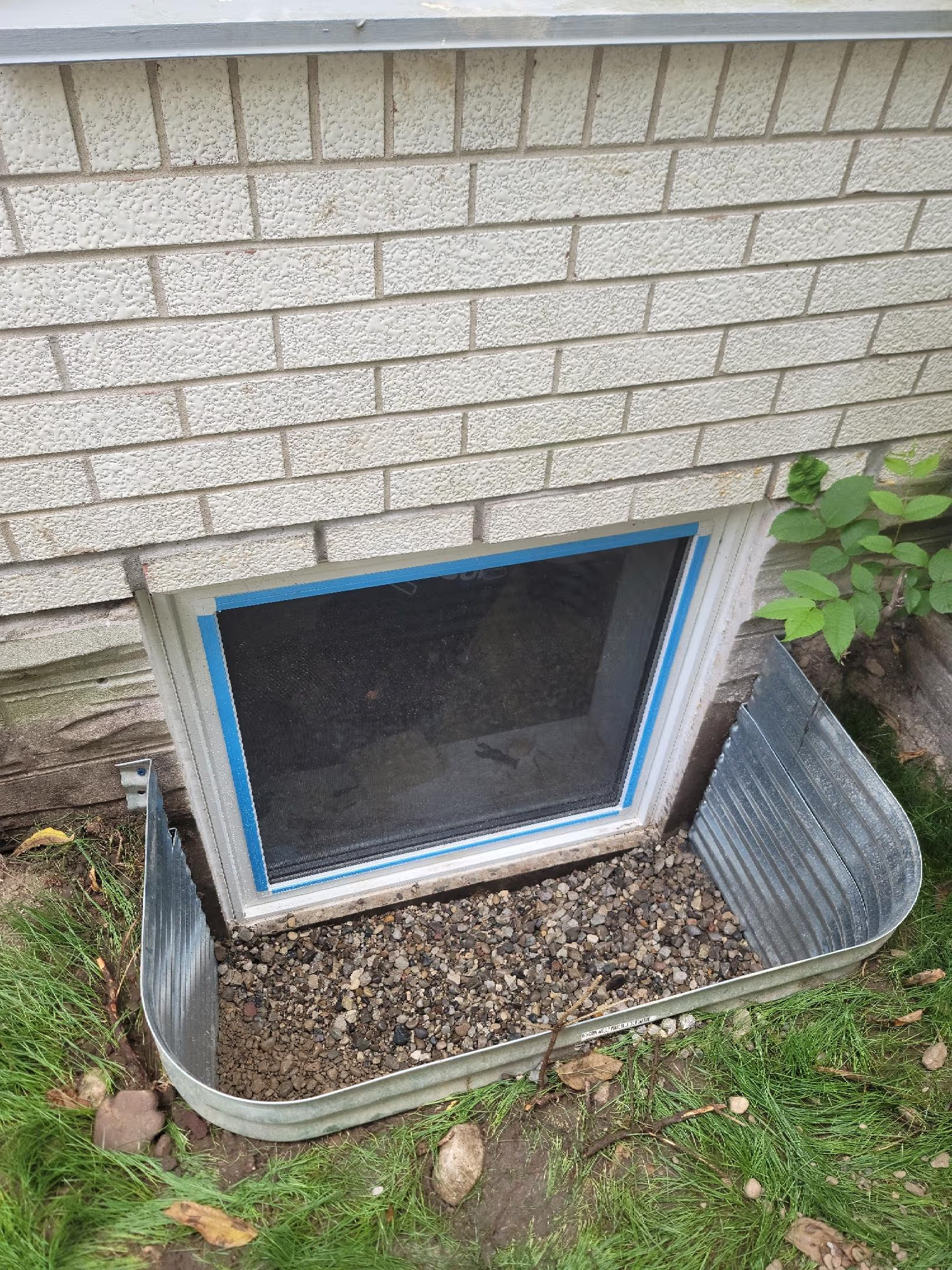 Metal window well installed around a basement window with gravel at the bottom for drainage and moisture protection.