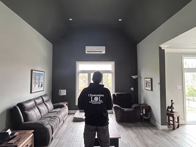 Contemporary living room with high ceiling, leather sofa, wall-mounted heat pump and large bright window with outdoor view.