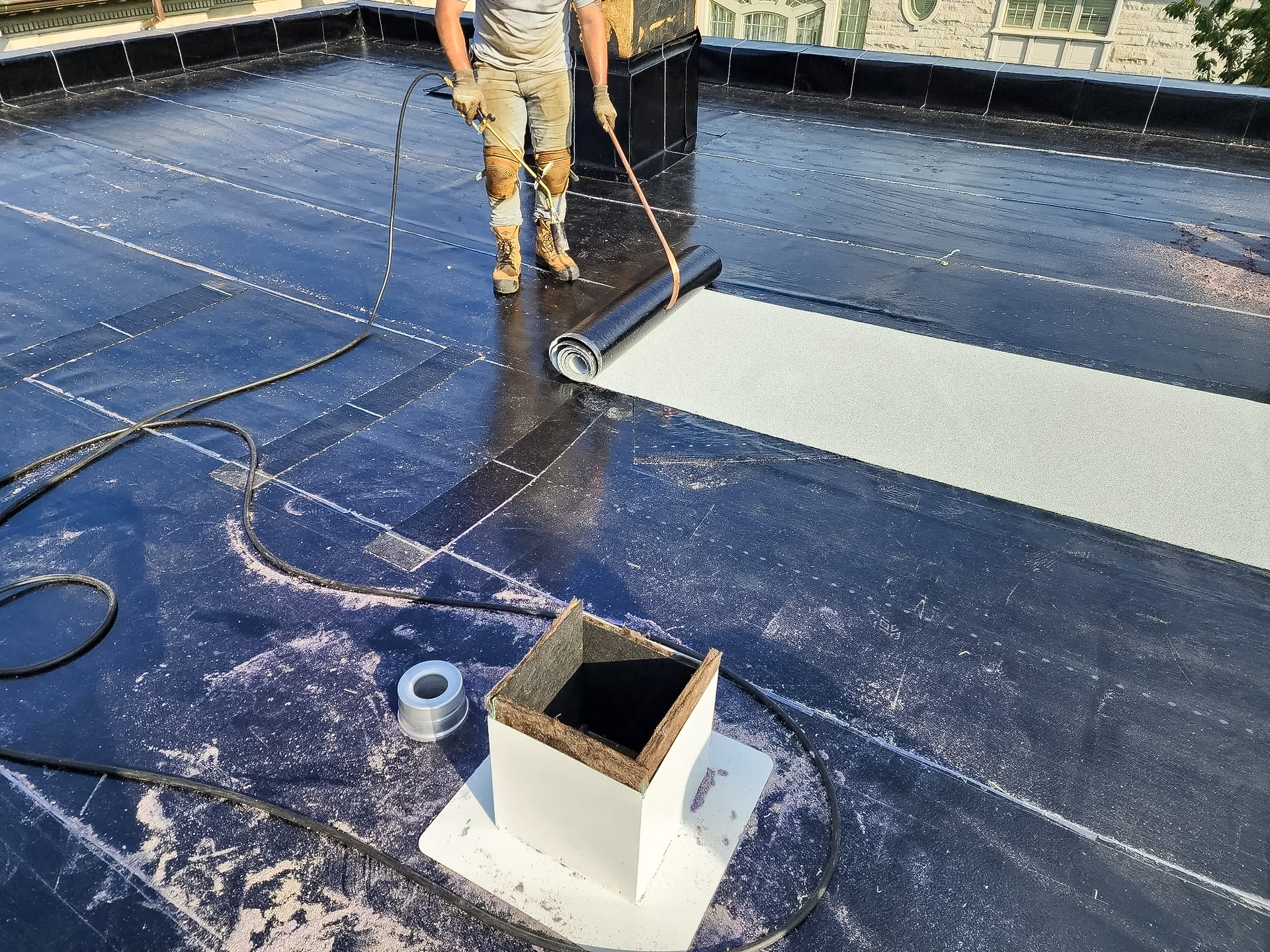 Installation work on an elastomeric membrane roof with a worker using a blowtorch.