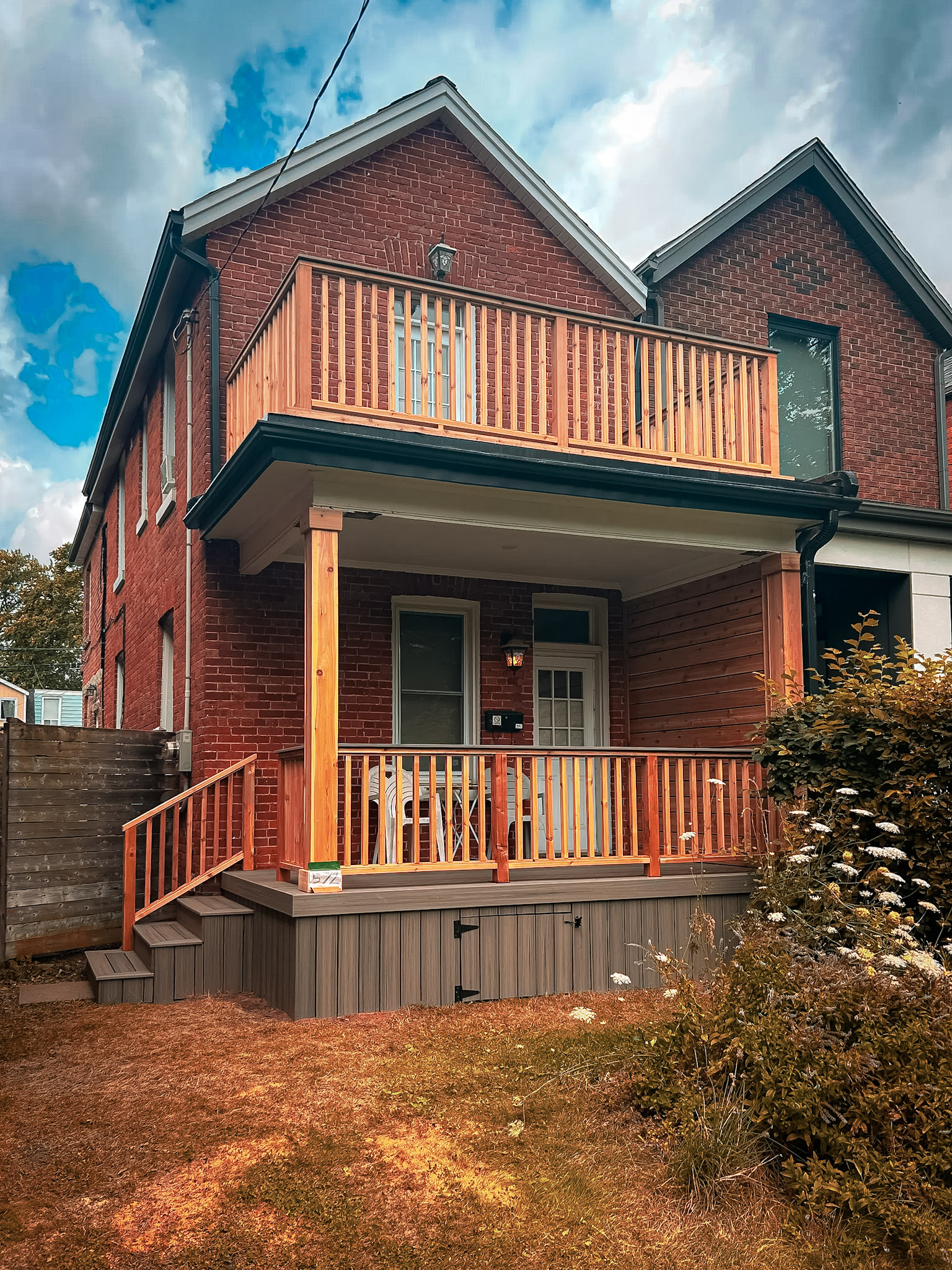 Maison en brique avec balcon et galerie en bois rénovés, garde-corps assortis et terrasse extérieure résidentielle.