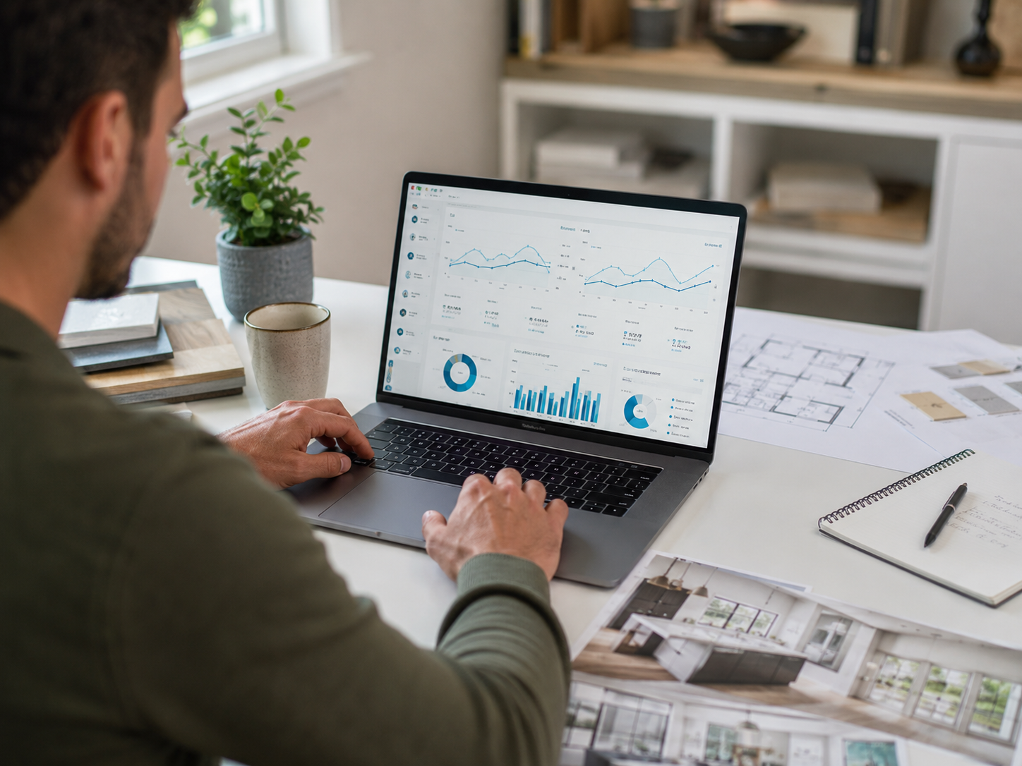 Professionnel analysant des données de performance sur un ordinateur portable, entouré de plans, d’échantillons de matériaux et de photos de rénovation intérieure.