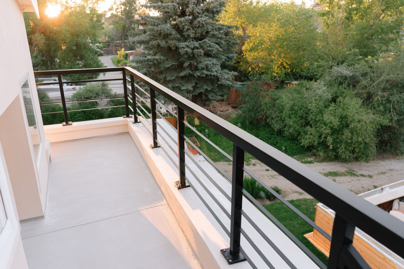Balcon moderne avec garde-corps en métal noir et vue sur un jardin boisé au coucher du soleil