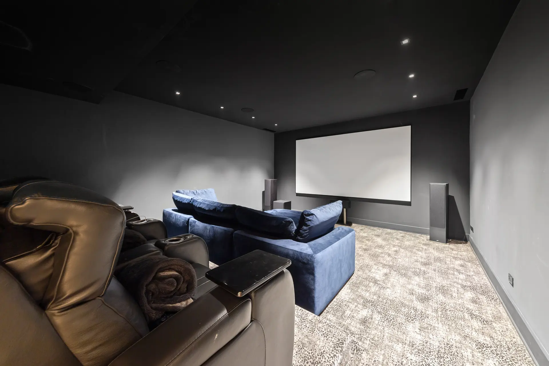 Modern home theater with large screen, reclining chairs, blue sofa, speakers and recessed lighting