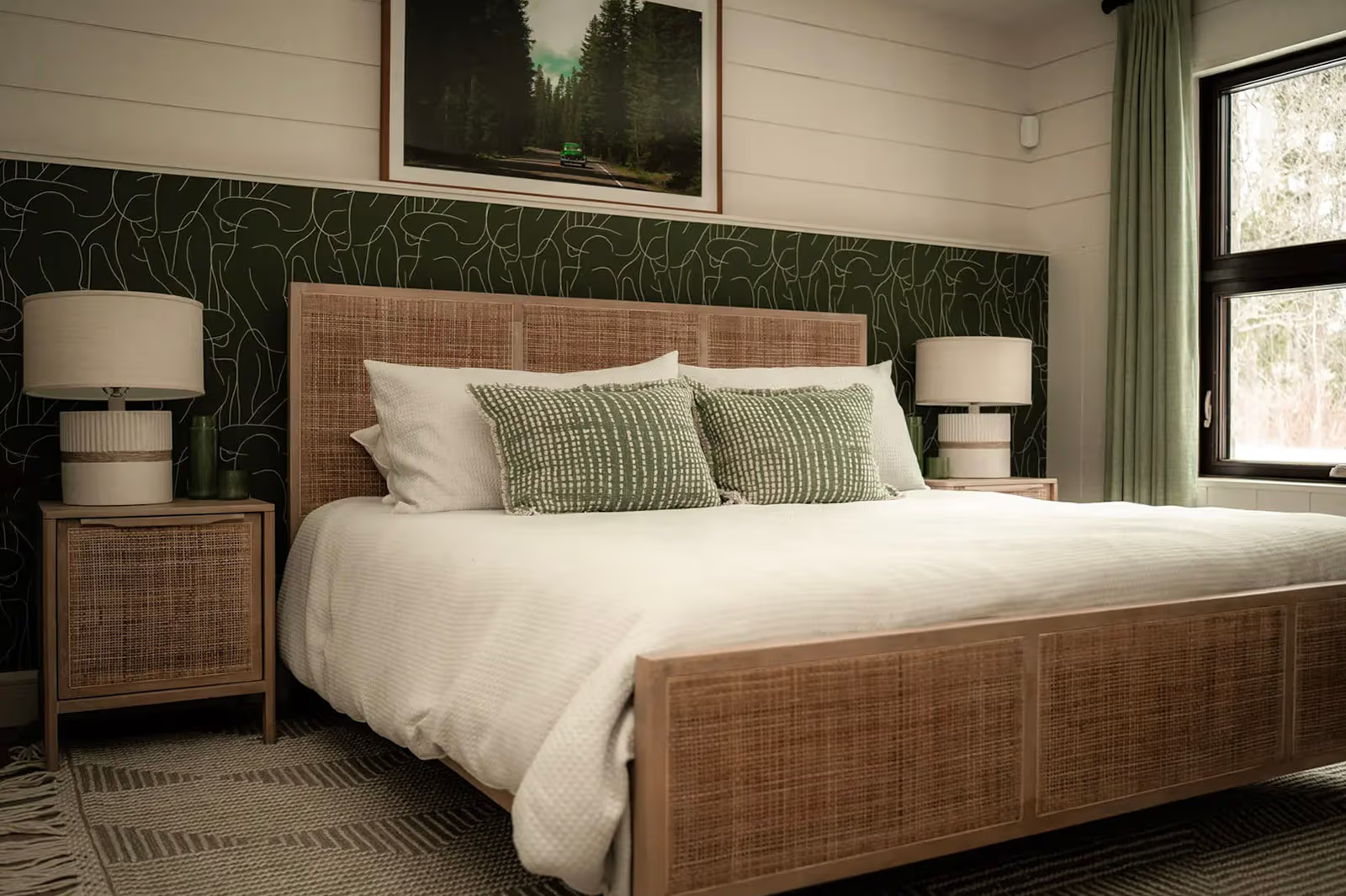 Chambre à coucher chaleureuse avec lit en rotin, papier peint vert à motifs, rideaux et décoration naturelle.
