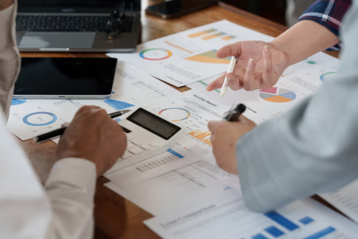 Équipe de professionnels analysant des rapports financiers avec graphiques, calculatrice et ordinateur portable sur une table de réunion.