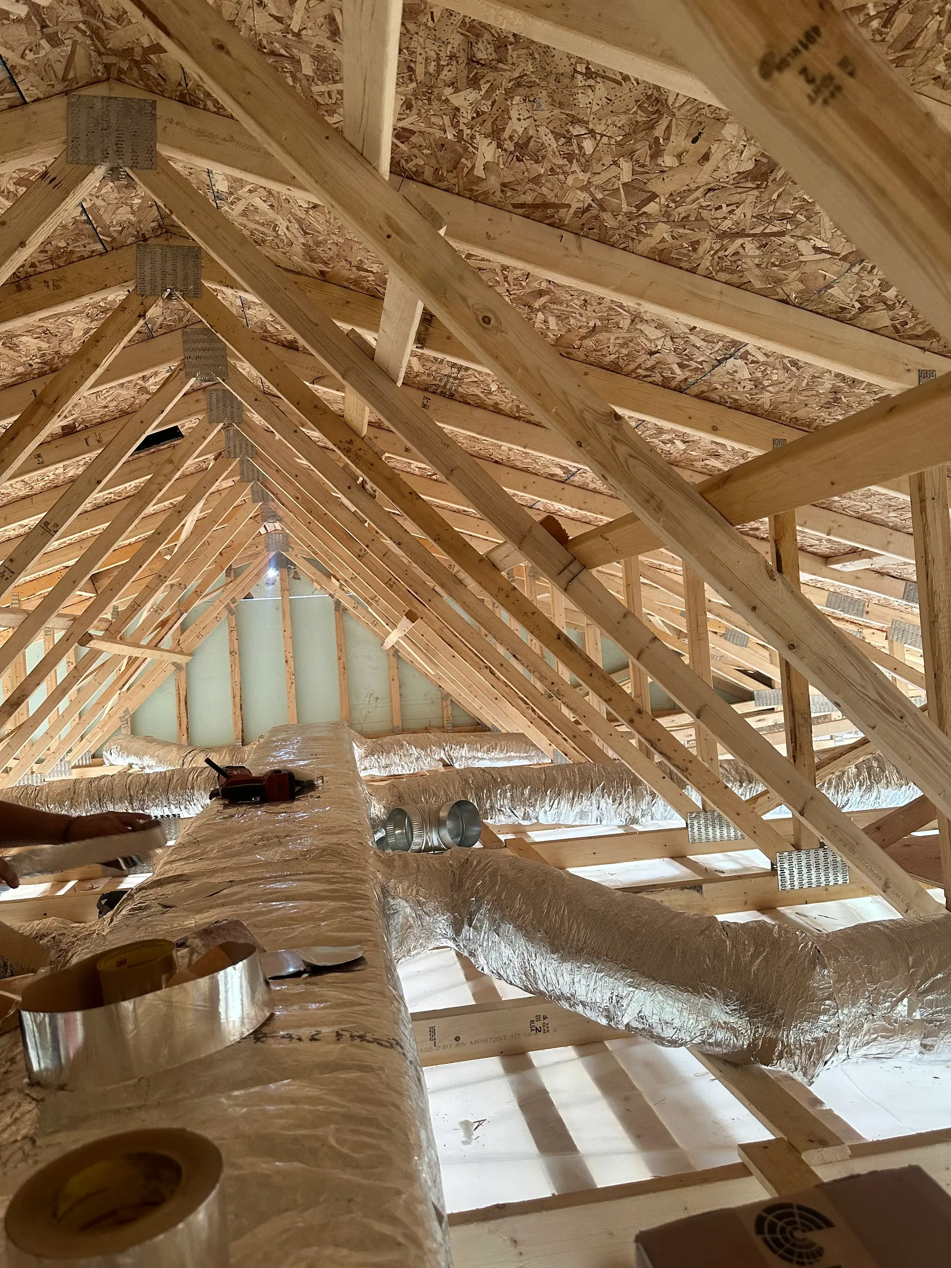 Charpente de toit en bois avec fermes préfabriquées, conduits de ventilation isolés et panneaux de toiture apparents dans un grenier résidentiel