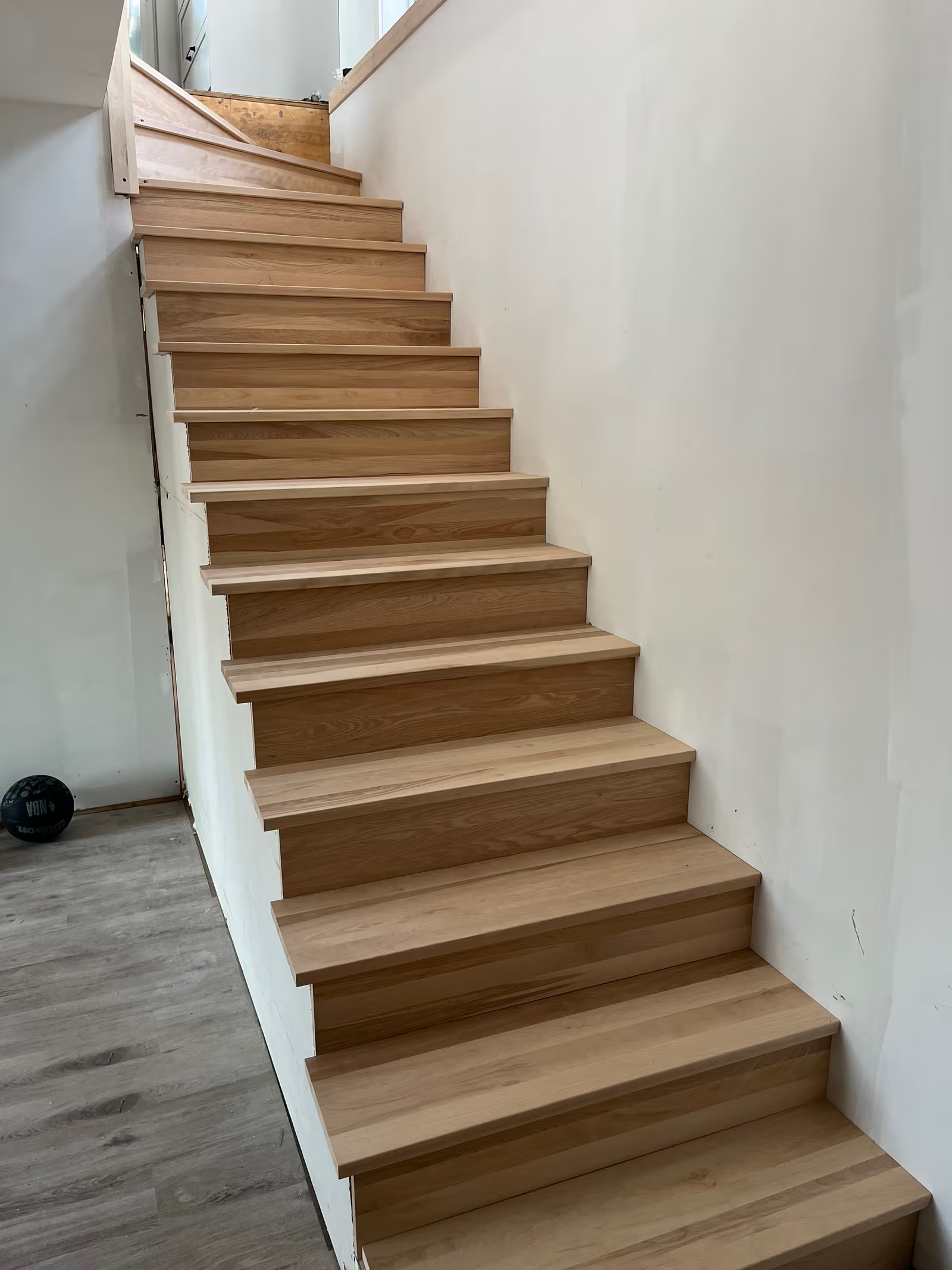Escalier intérieur en bois naturel installé entre deux murs blancs dans une maison en rénovation