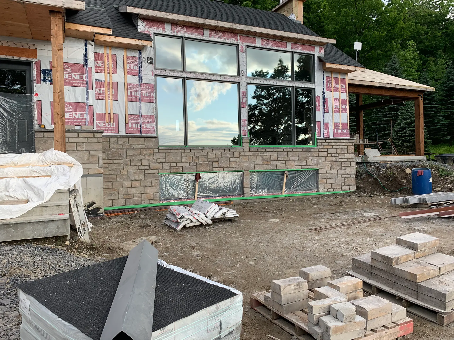 House under construction with partially installed stone siding, large windows, and construction materials on the ground