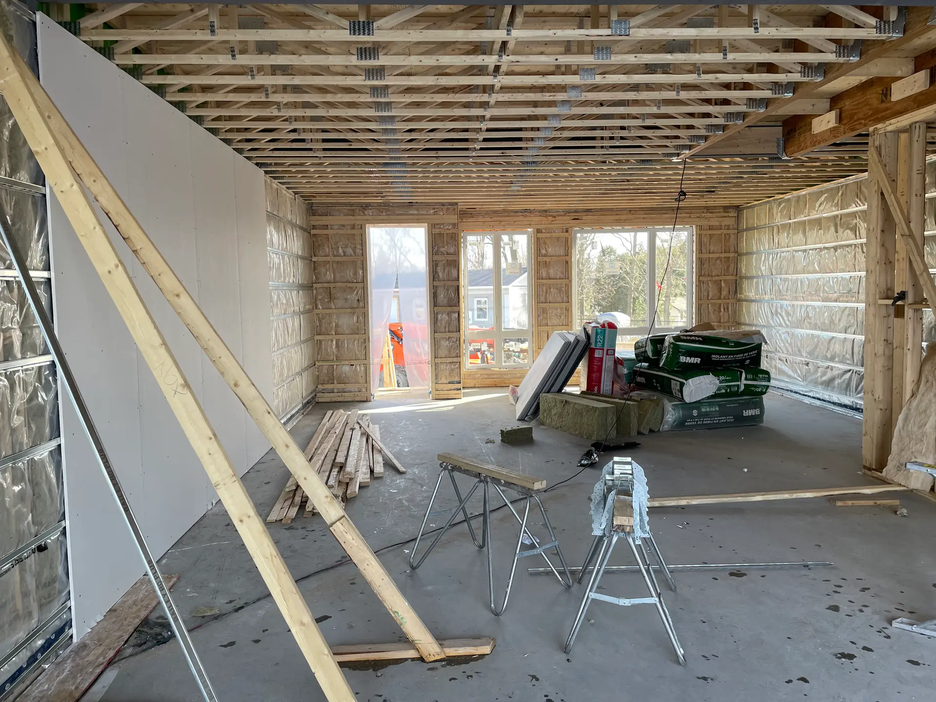 Grand espace intérieur en construction avec ossature de bois, poutrelles apparentes, murs isolés, panneaux de gypse et matériaux de rénovation