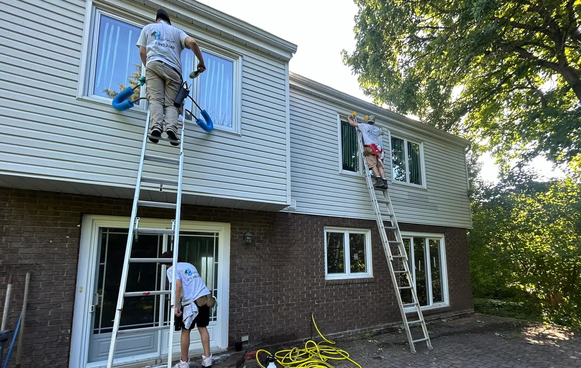Équipe de techniciens travaillant sur échelles pour l’entretien des fenêtres et du revêtement extérieur d’une maison