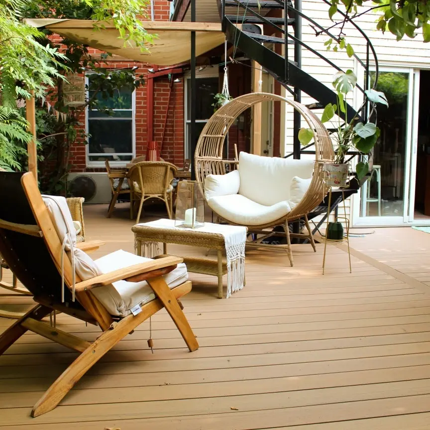 Terrasse en bois avec mobilier en rotin, chaise suspendue, fauteuil en bois et décoration végétale, créant une ambiance chaleureuse et relaxante.